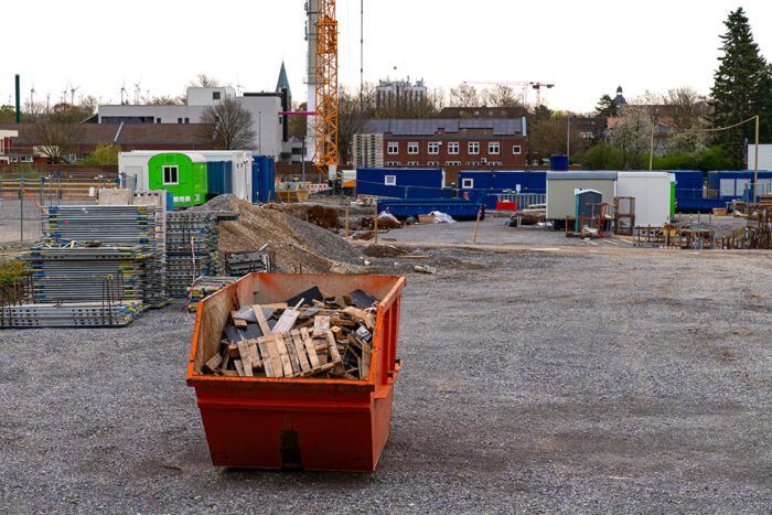 Orange metal container for collecting waste and stacked scaffolding at a construction site.