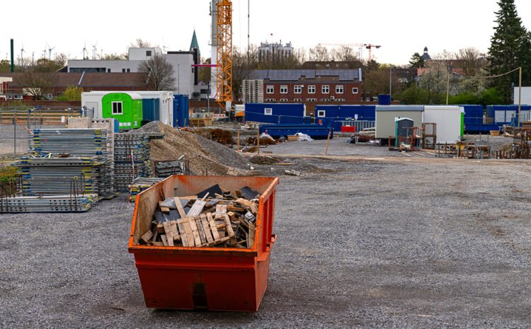 Orange metal container for collecting waste and stacked scaffolding at a construction site.